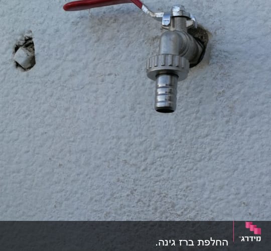 ברז מתכת עם ידית אדומה על קיר